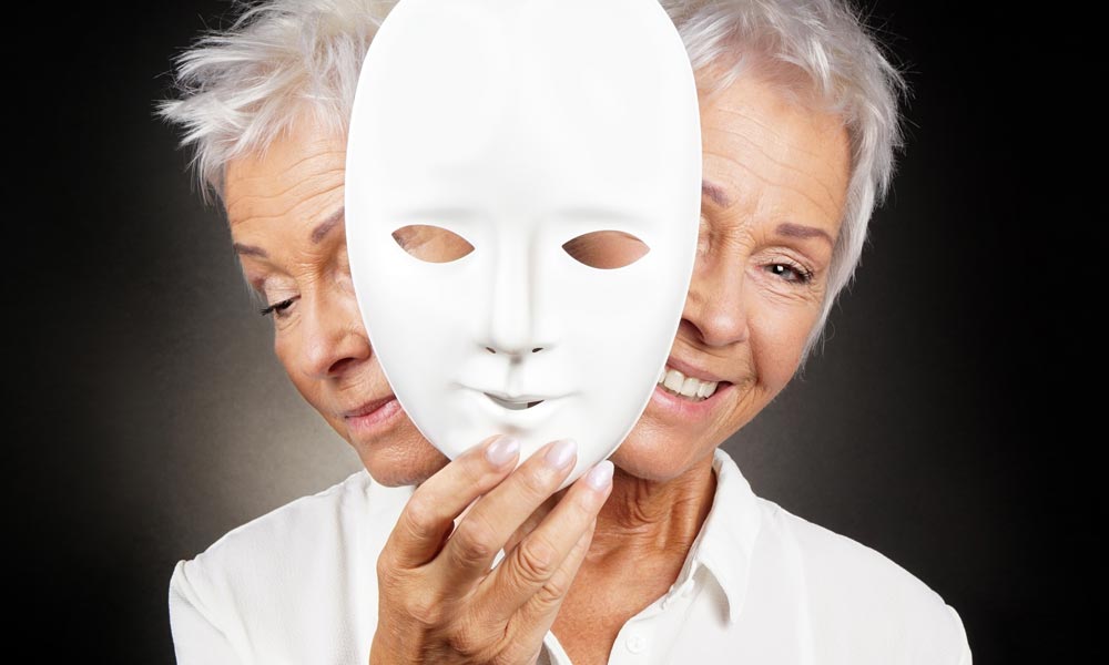 two-faced older woman both sad and happy holds a mask