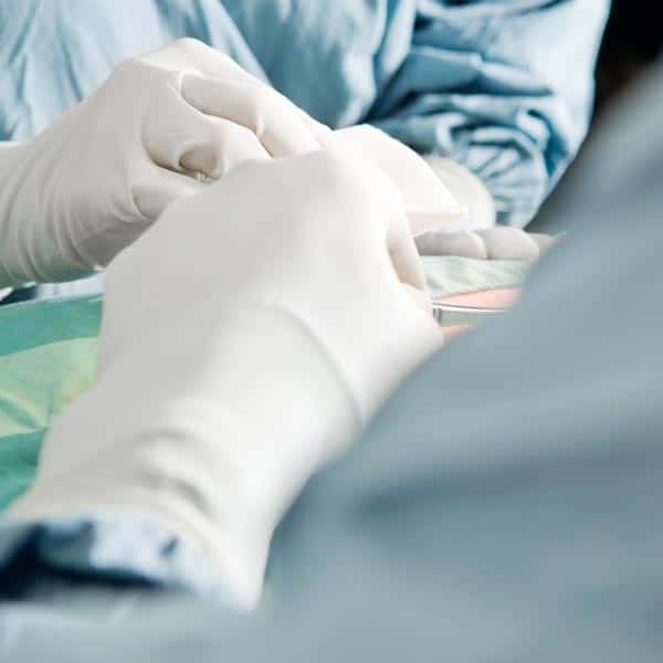 surgeons in operating room with white gloves and scalpel making an incision