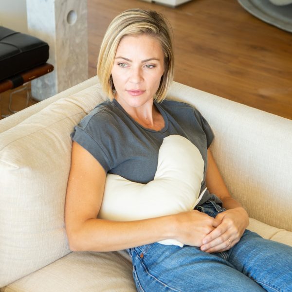 woman on couch with billow heart pillow to support right arm